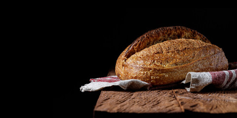 Fototapete - Rustic sourdough wheat bread on a wooden table and on a black background.