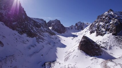 Wall Mural - High snow-capped mountains among glaciers. Aerial view from a drone on a rocky gorge. The glacier is covered with snow and rocks. The sky is blue and the sun is shining brightly. The ice is cracking