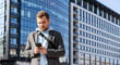 © Barillo Images - Man using his mobile phone online messaging standing on street against urban building.