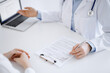 © rogerphoto - Doctor and patient sitting opposite each other at the desk in clinic. The focus is on female physician's hands pointing into laptop computer monitor, close up. Medicine concept