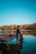 © Marija - Young woman standing on lake pier and enjoying in beautiful landscape.