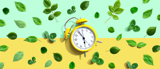 Wall Mural - Yellow vintage alarm clock with green leaves - flat lay