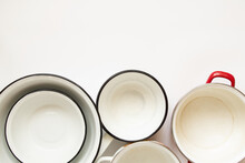 Various Used Enamel Kitchen Pots On A White Background, A Set Of Pots And A Bowl