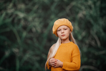 Portrait of a Beautiful stylish blonde girl in a yellow beret and jacket on a green background on the street