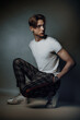 male fashion model crouch and pose deliberate in studio, showcasing his chiseled features and impeccable style while his confident gaze exudes a sense of cool sophistication and look to right side