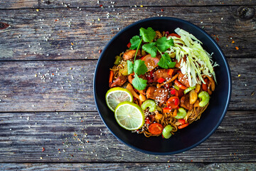 Asian food - chicken nuggets, noodles, stir fried vegetables, soy sauce, cabbage and shimeji mushrooms on wooden table
