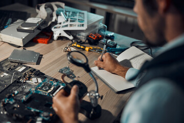 Poster - Technician, engineer or IT man repair motherboard, circuit board or electronic device in workshop or office at night. Person, startup and guy writing hardware notes for computer or technology in lab