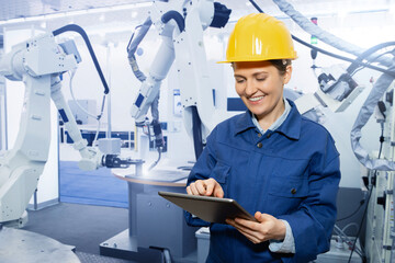 Wall Mural - Woman engineer uses a digital tablet to control robots in a smart factory. Smart industry 4.0 concept	