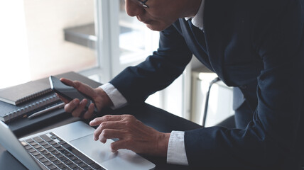 Wall Mural - Asian businessman working on laptop computer on table office, closeup. Business man using mobile phone and typing on laptop, searhing the information, internet networking, corporate business