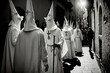 Procession of hooded Nazarenes marching through streets in the Spanish Holy Week, carrying crosses to commemorate the Passion of Christ. Traditional religious event full of devotion. Generative AI.