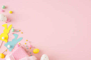 Easter party concept. Flat lay photo of yellow white eggs gift box paper bunny toppers and chocolate sprinkles on isolated pastel pink background with copyspace