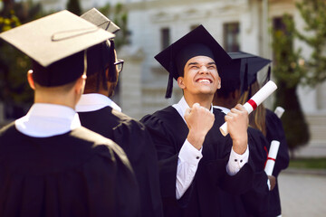 I did it. Happily excited male student clenched his fist with joy during graduation ceremony. Guy in academic mantle and mortarboard has just received diploma and is ready for next step in his life.