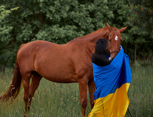 Canvas Print - A girl with a frag of Ukraine stands near a red horse