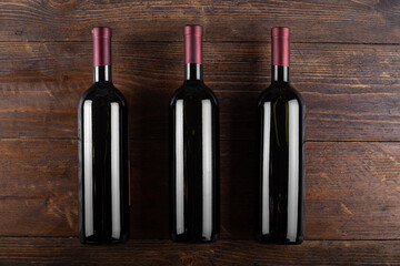 Wall Mural - Three bottles of red wine on a wooden background. View from above.