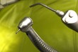 Dental stomatology drill head with ball shaped diamond bur attached, 3-way air-water-mist syringe head and light green dental chair in background