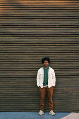 Canvas Print - Young cool African American hipster teen guy standing at wooden wall background. Stylish trendy gen z teenage student model looking at camera for authentic portrait outdoors. Vertical full length shot