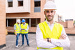 © Xavier Lorenzo - Successful portrait of young confident engineer architect standing at building construction with two worker people discussing on the background