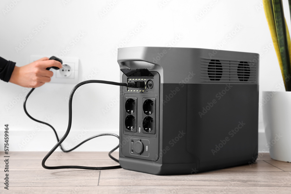 Woman inserting plug of portable solar station into socket at home