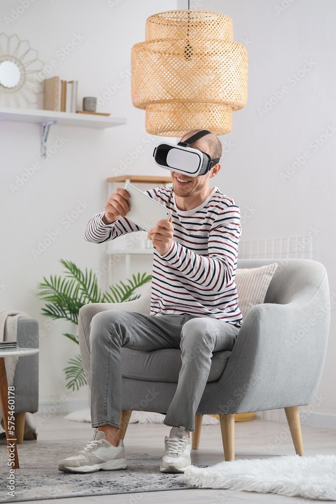 Young man with VR glasses and tablet computer at home