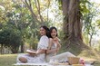 © Natee Meepian - Charming beautiful young Asian woman in a lovely dress, holding a flower bouquet, enjoying a picnic with her friend in the park
