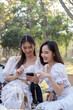 © Natee Meepian - Relaxed Asian women in beautiful dresses are watching a video on a mobile phone togetherthey are having picnic,they talk happily