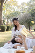 © Natee Meepian - Two young Asian women beautiful read a book while picnicking in the beautiful garden together on the weekend