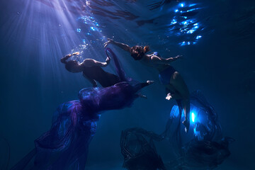 two girls are swimming in a pool under the water with a fashion fabric on a dark blue background like in the sea