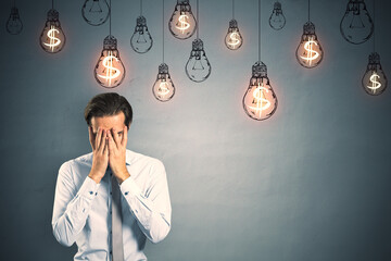 Poster - Stressed young european businessman standing on concrete wall background with glowing lamp sketches and dollar sign. Business ideas, income and success concept.