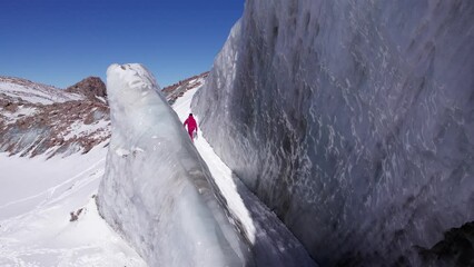 Wall Mural - A climber walks on a large glacier in the mountains. A high frozen wall of ice similar to marble. Unusual coloring is gray-white with streaks. The glacier is collapsing. Lots of snow. Blue sky. Almaty