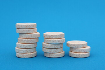 Large round yellow pills are stacked in ascending order on a blue background.