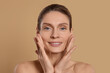 © New Africa - Woman massaging her face on beige background