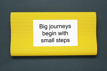 Wall Mural - Card with phrase Big Journeys Begin With Small Steps on dark background, top view. Motivational quote