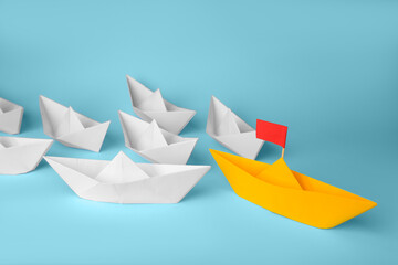 Wall Mural - Group of paper boats following yellow one on light blue background. Leadership concept