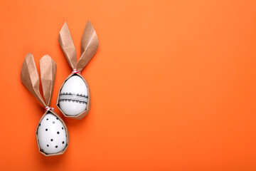 Wall Mural - Easter bunnies made of craft paper and eggs on orange background, flat lay. Space for text