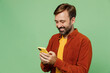 © ViDi Studio - Elderly smiling happy man 40s years old he wears casual clothes red shirt t-shirt hold in hand use mobile cell phone browsing internet isolated on plain pastel light green background studio portrait.