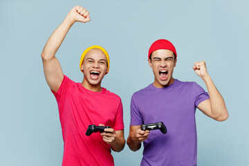 Sticker - Young excited couple two friends men wear casual clothes together hold in hand play pc game with joystick console do winner gesture isolated on pastel plain light blue cyan background studio portrait.