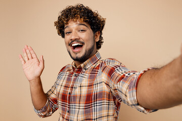 Close up smiling happy Indian man wear shirt casual clothes doing selfie shot pov on mobile cell phone wav hand isolated on plain pastel light beige background studio portrait People lifestyle concept