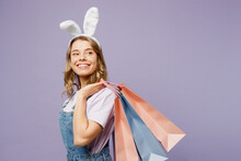 Side View Young Woman Wears Casual Clothes Bunny Rabbit Ears Hold Paper Package Bags After Shopping Isolated On Plain Light Pastel Purple Background Studio Portrait. Happy Easter Sale Buy Day Concept.
