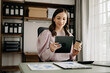 © Nuttapong punna - Confident business expert attractive smiling young woman typing laptop ang holding digital tablet  on desk in office.