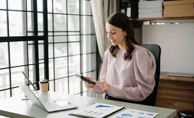 Confident business expert attractive smiling young woman typing laptop ang holding digital tablet  on desk in office.