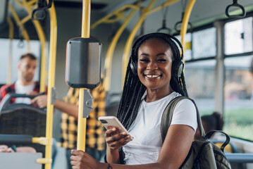 Wall Mural - African american woman riding in a bus and using a smartphone and headphones