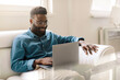 © Prostock-studio - Happy african american businessman sitting in office on couch, working on laptop computer and smiling, copy space