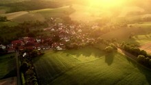 Flying Over Idyllic Rural Landscape With A Small Village In Nature, Dived In Beautiful Warm Rays Of Golden Morning Light After Sunrise


