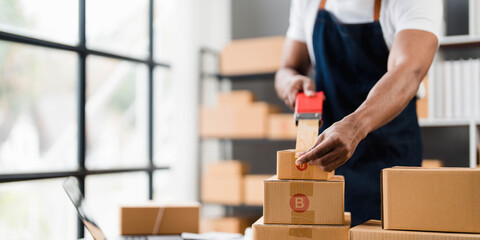 Photo of young entrepreneur man packing he goods while sitting in table comfortable sitting room as background. Shipping, Shopping online, Small business entrepreneur, SME, freelance.