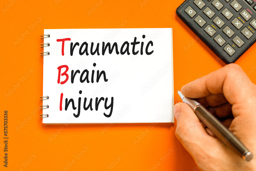 TBI traumatic brain injury symbol. Concept words TBI traumatic brain injury on white note on a beautiful orange background. Doctor hand. Medical and TBI traumatic brain injury concept. Copy space.