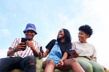African American Man Using His Cell Phone And Laughing Together With His Two Female Friends Outdoors