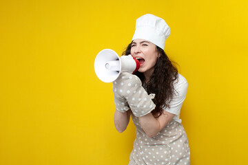 Wall Mural - girl chef in apron and baking gloves holds megaphone and announces information on yellow background