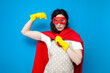 girl cleaner in superman costume shows strength on blue background, woman housewife in superhero mask shows biceps