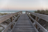 Fototapeta Natura - Straight wooden pathway with railings in between sand dunes against the ocean and horizon sky. Wooden walkway near the protected sand dune with grasses with views of ocean waves in Destin, Florida.