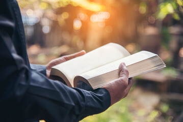 Poster - Asian man holding book reading magazine at green park in natural garden. Young man relaxation read open book self study. University men happy learning. Closeup Men hands open textbook in green park